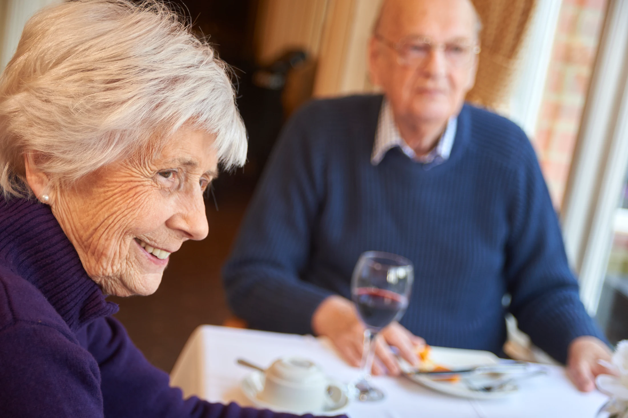 An older woman smiling over a meal with another resident
