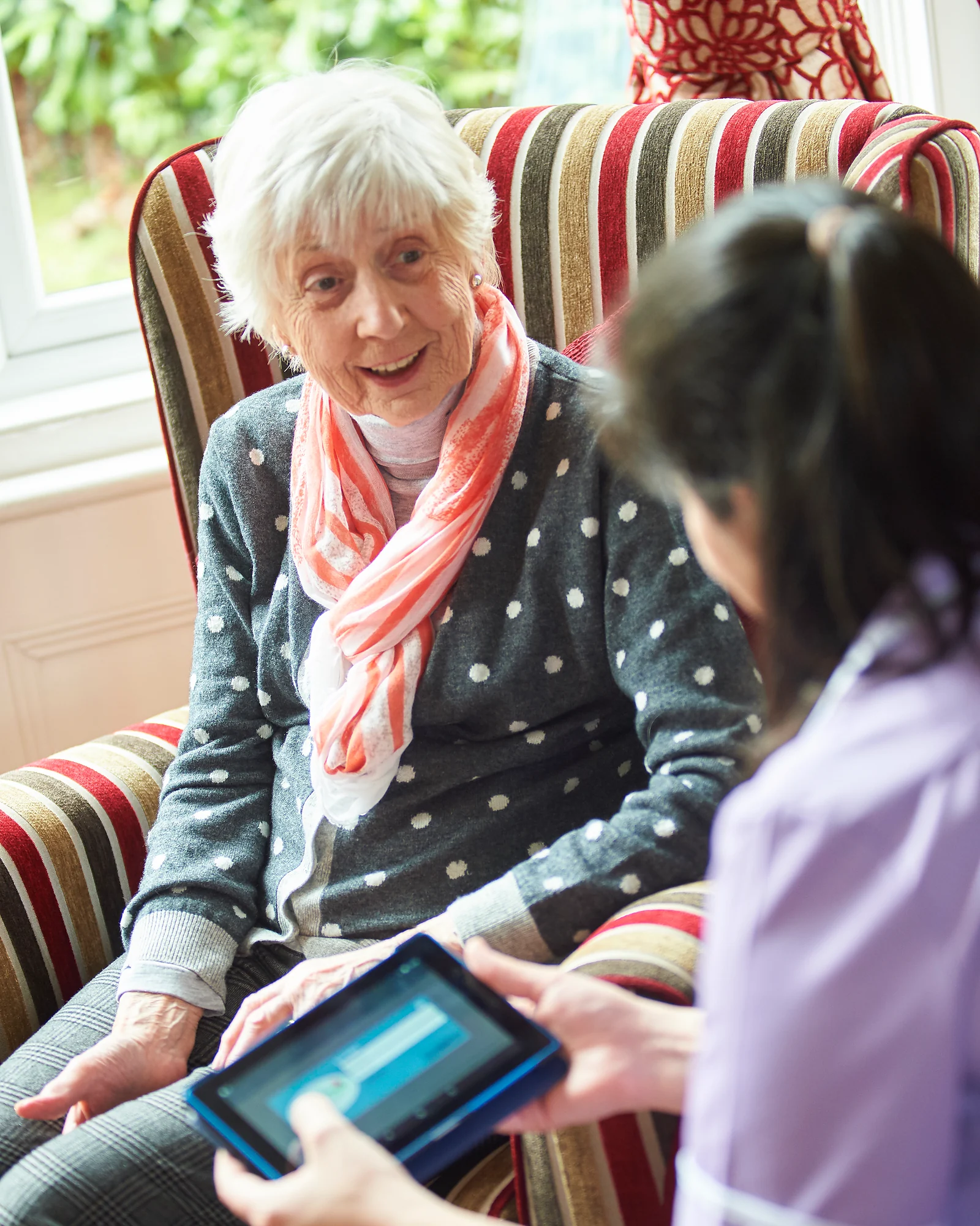 An older woman smiling as she talks with a care professional using a tablet