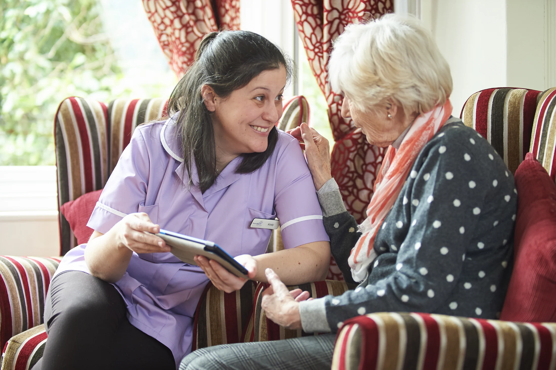 A care professional and an older woman sharing a warm conversation while using a tablet