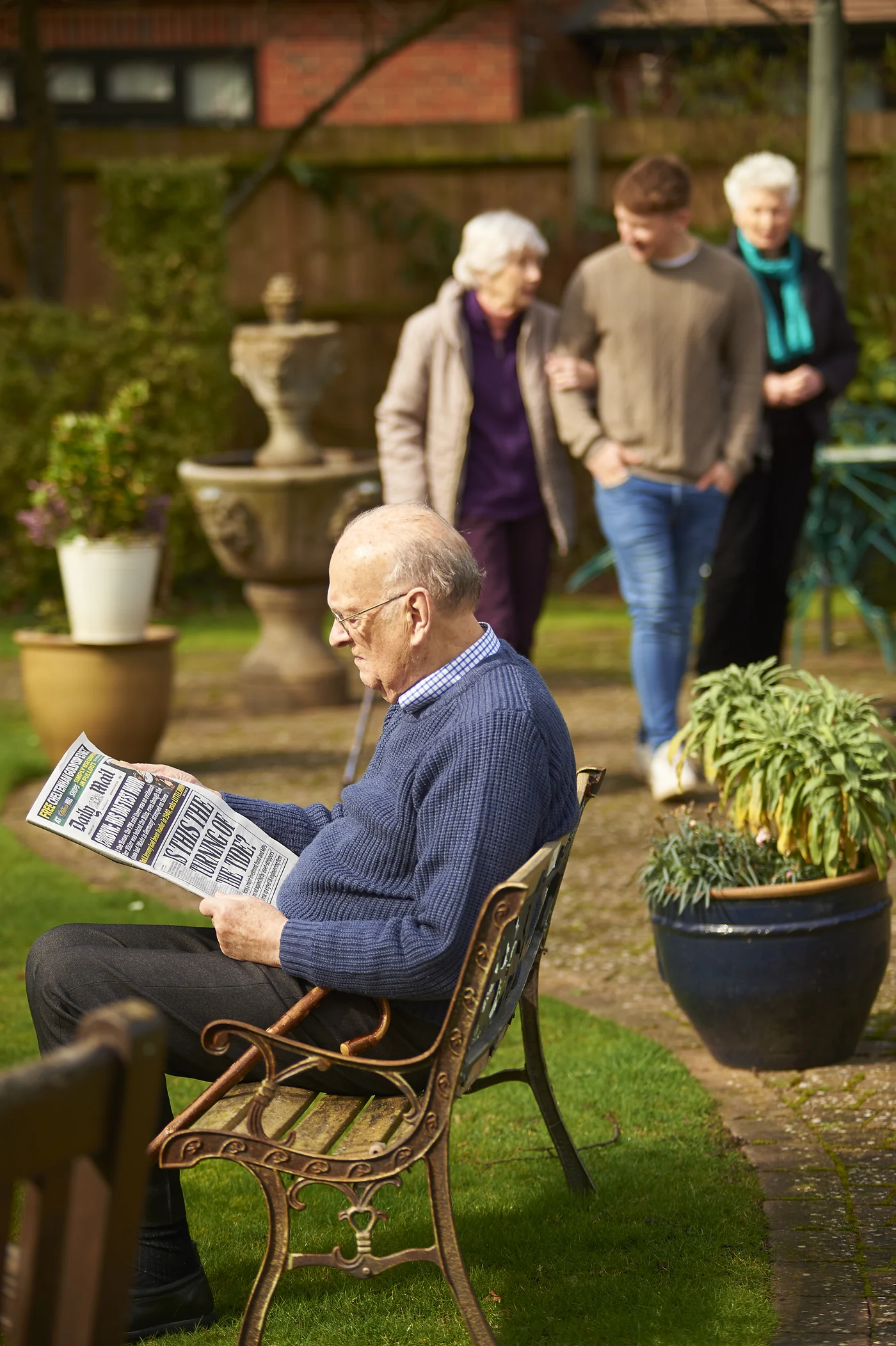 A Nettlestead resident reading in the garden while others walk nearby