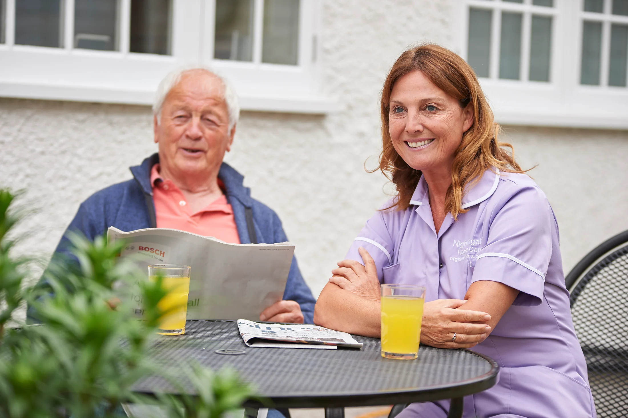 An older man and a care professional sitting together in a garden