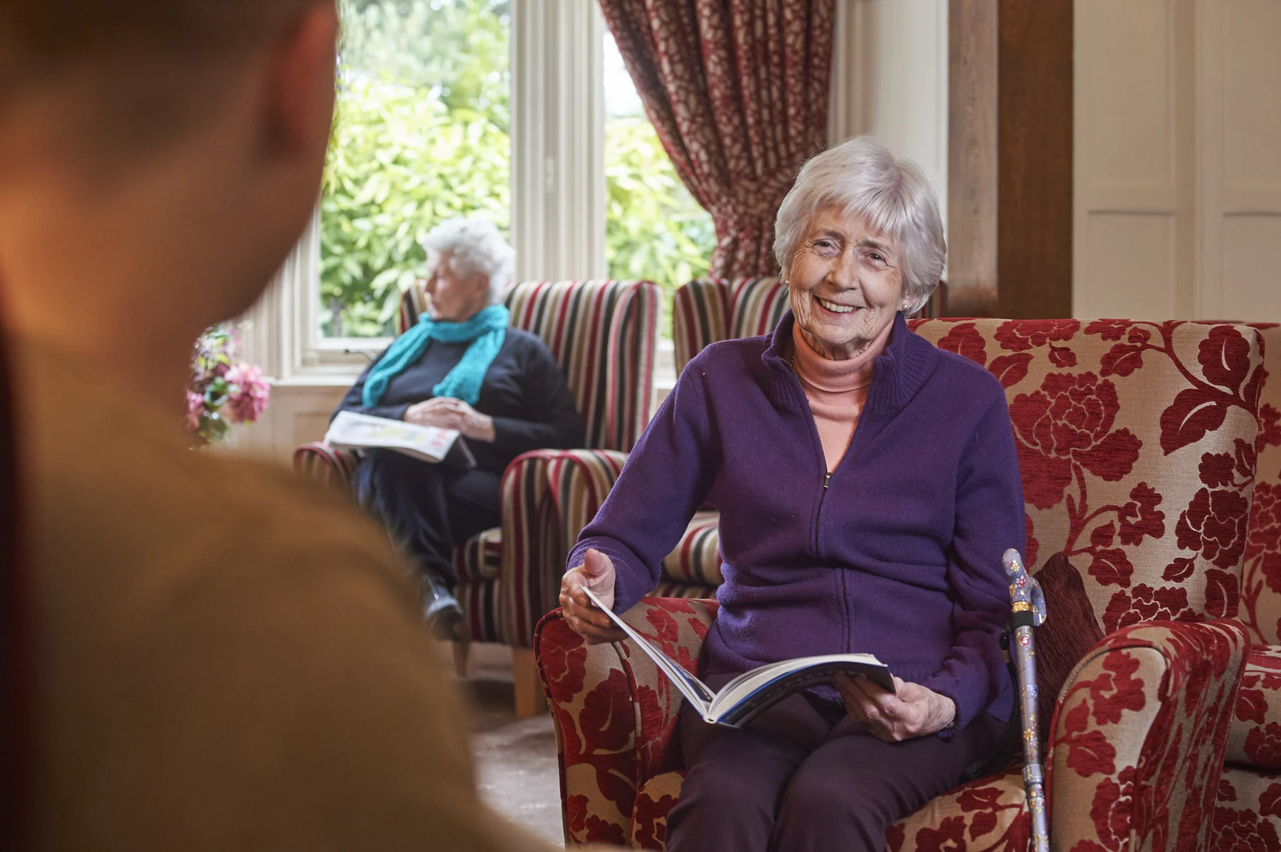 A Nettlestead resident smiling with a book while enjoying company in the lounge