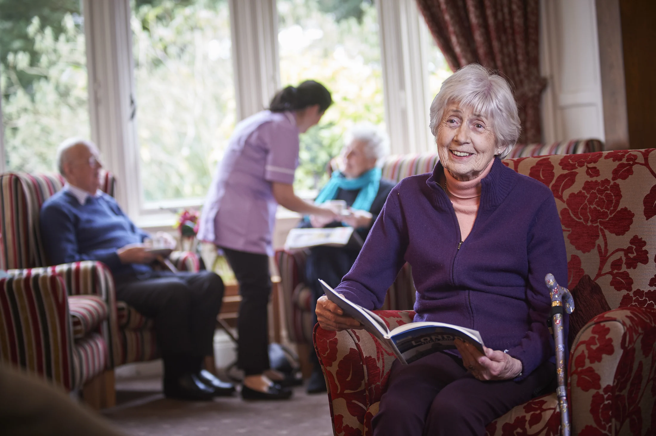 A Nettlestead resident relaxing with a book while members of the care team support others nearby